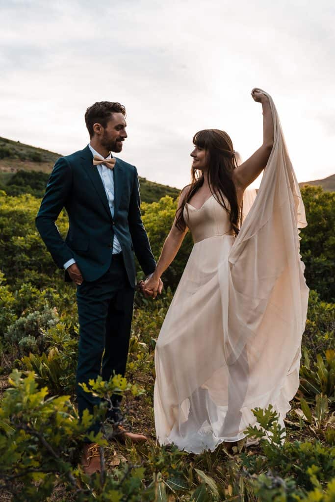 couple holding hands and bride playing with dress while they smile at each other