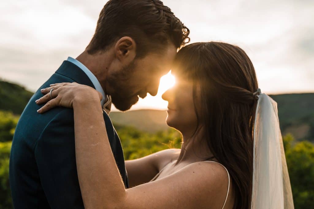 couple facing each other with their foreheads touching and the sun gleaming through behind them