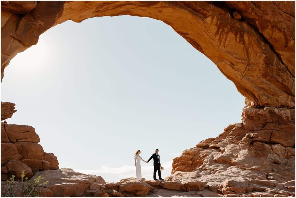 beautiful big shot of the couple in an arch. holding hands on their moab elopement.