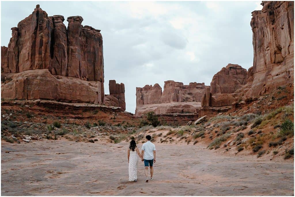 Sunrise photoshoot of couple walking away from the camera on their adventure session in the arches national park