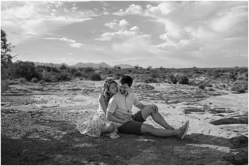 photo of couple sitting on ground and hugging on their adventure session in the arches national park in black and white