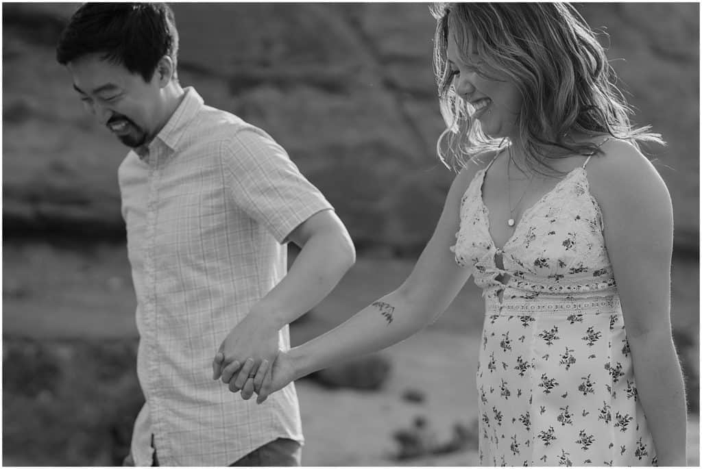 black and white photo of couple holding hands and smiling on their adventure session in the arches national park