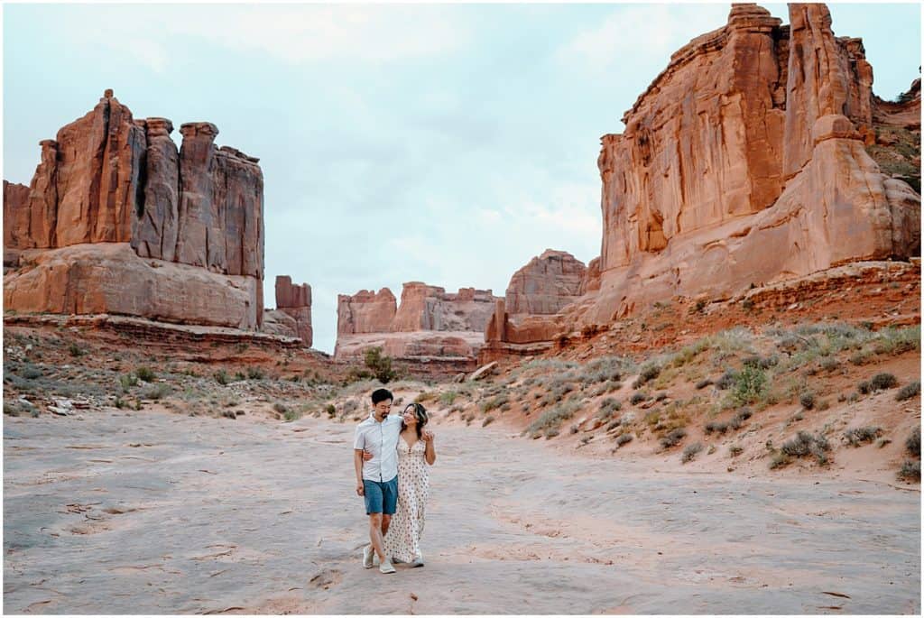 sunrise photoshoot of couple embracing and walking towards camera on their adventure session in the arches national park