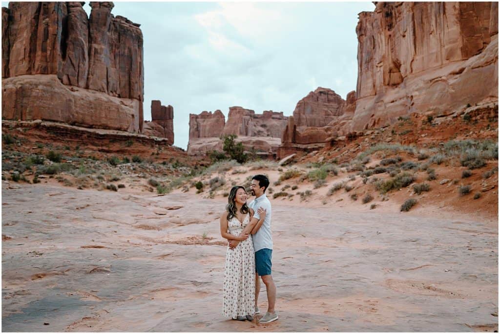 sunrise photoshoot of couple embracing and walking towards camera on their adventure session in the arches national park