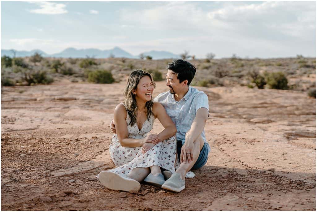 photo of couple sitting on ground and hugging on their adventure session in the arches national park