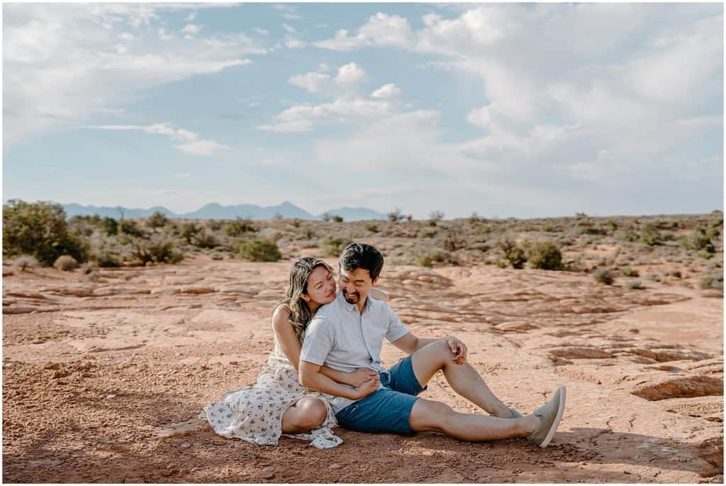 photo of couple sitting on ground and hugging on their adventure session in the arches national park