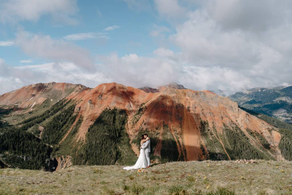 The bride and groom embrace each other against the backdrop of a red and green mountain during their Colorado elopement ceremony. 