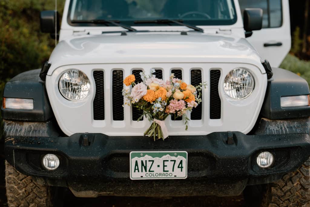 Elopement flowers are shown displayed on the front bumper of a Colorado jeep during a bride and groom's colorado mountain wedding in Ouray. 