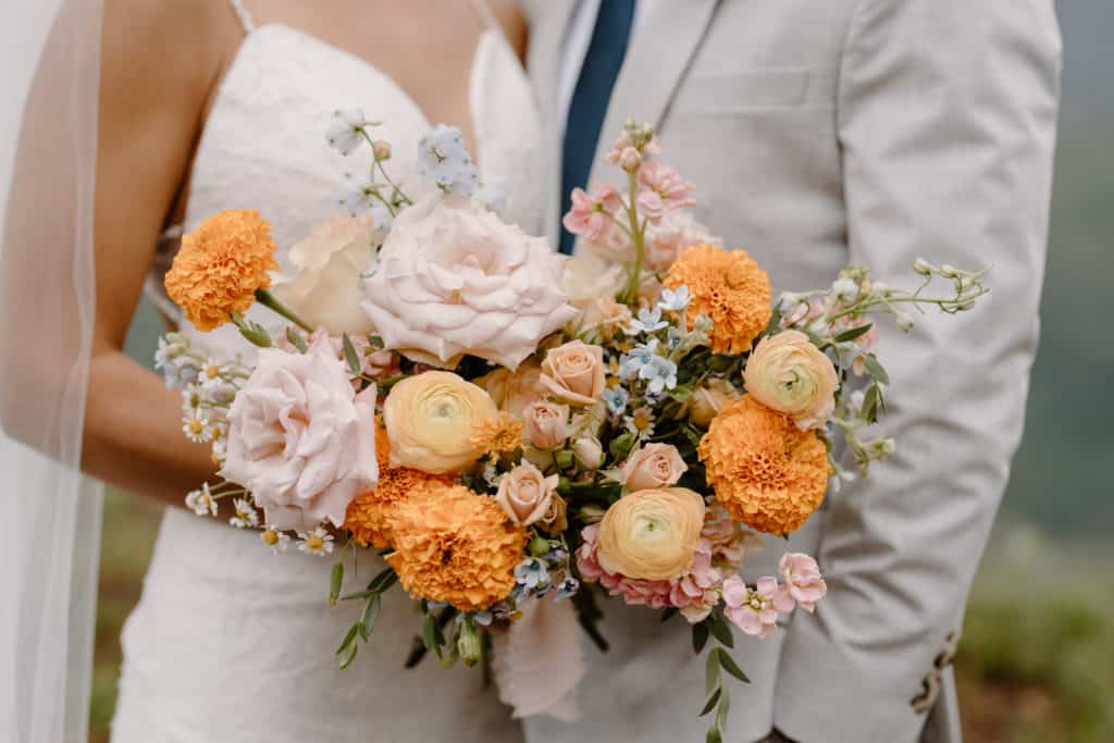 This image shows a close-up shot of a gorgeous orange, pink, and white bouquet–the bride's choice of florals for their San Juan Mountain elopement. 