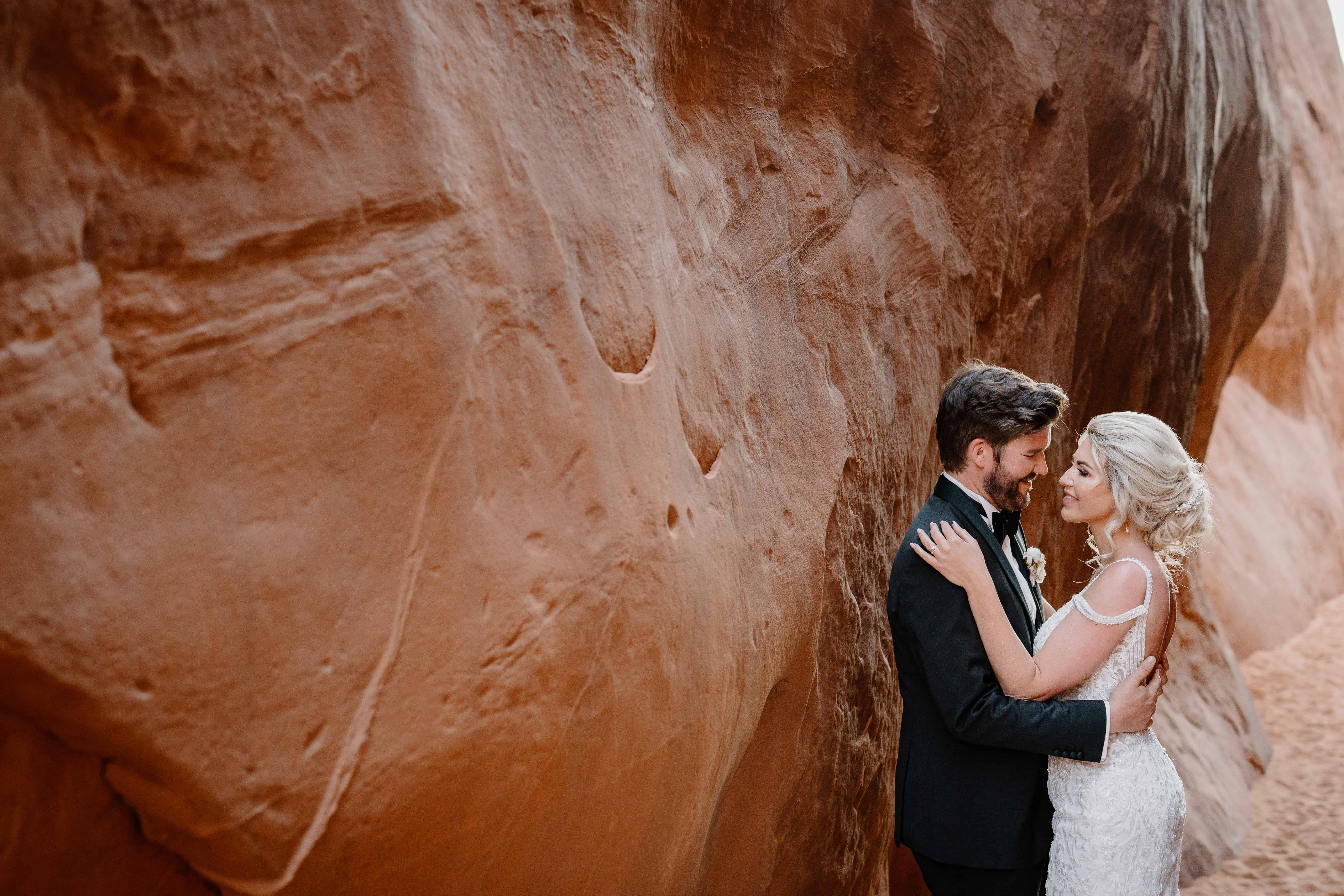 A couple holds each other close near the sand wall of an ancient arch during their Moab, Utah wedding ceremony. 