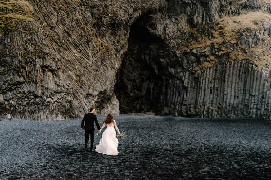 A couple runs off into the distance, their wedding attire breezing behind them in the wind during their iceland elopement ceremony. 