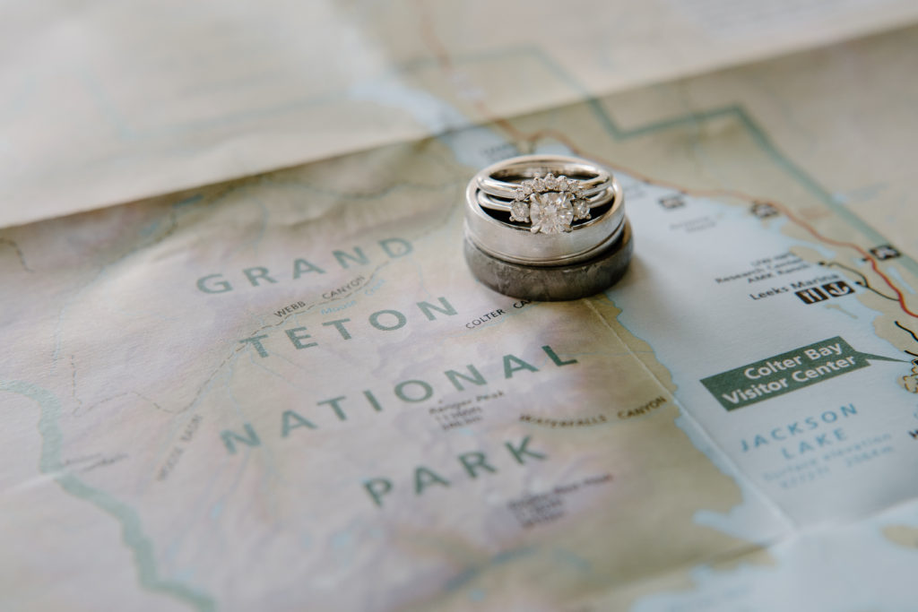 A stack of engagement and wedding rings lies on top of a map of the Grand Teton National Park, where a young couple eloped. 