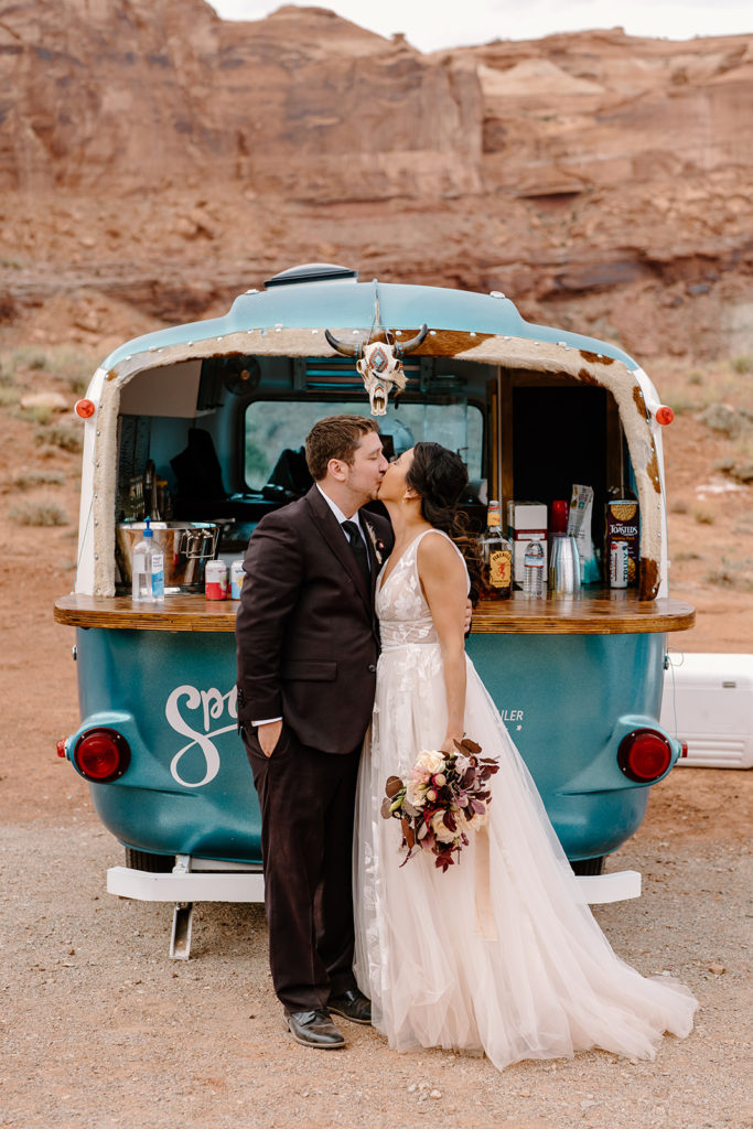 A couple kisses in front of their adorable bar cart in the middle of the desert, a feature their elopement photographer and their wedding coordinator helped orchestrate. 