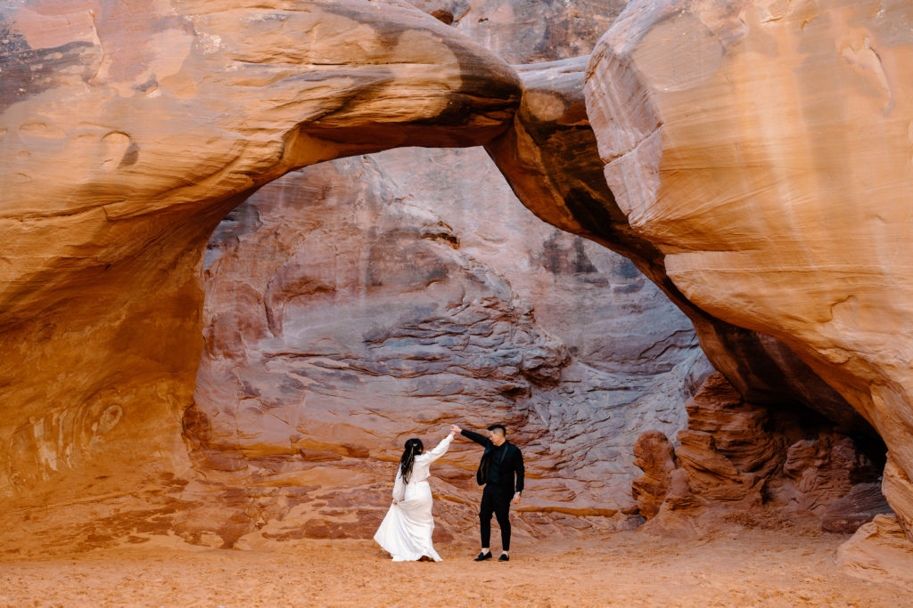 A bride and groom dance beneath a gorgeous Utah arch during their Moab adventure elopement. 