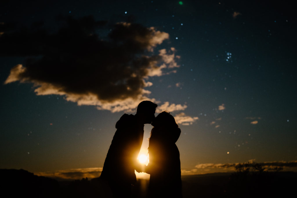 The moon rises between a kissing bride and groom during their Moab adventure elopement, showing only their silhouettes against the gorgeous sky. 