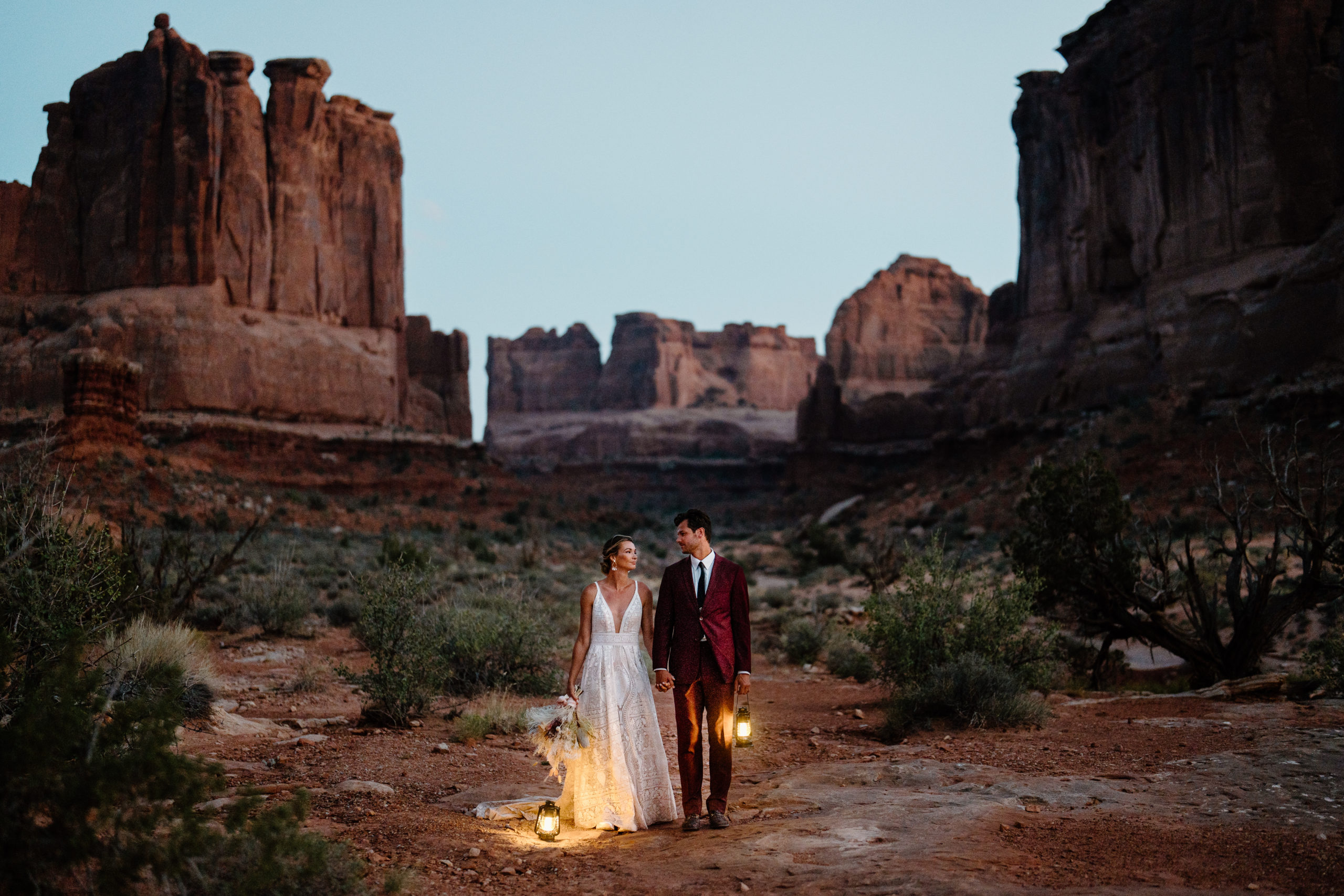 A bride and groom hold hands as they walk through the Utah desert, exploring on the day of their Utah adventure elopement.