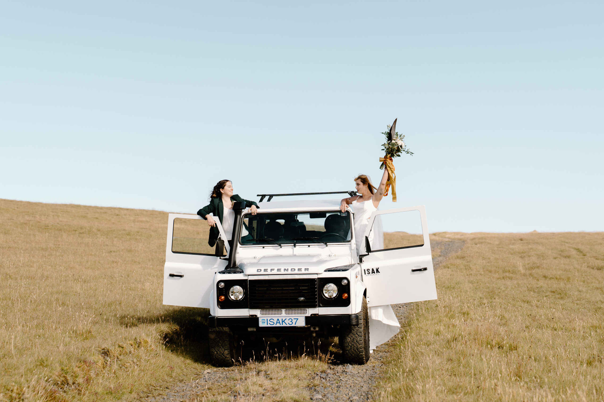Two brides hang out the windows of a cool offroad vehicle during their intentional wedding ceremony.