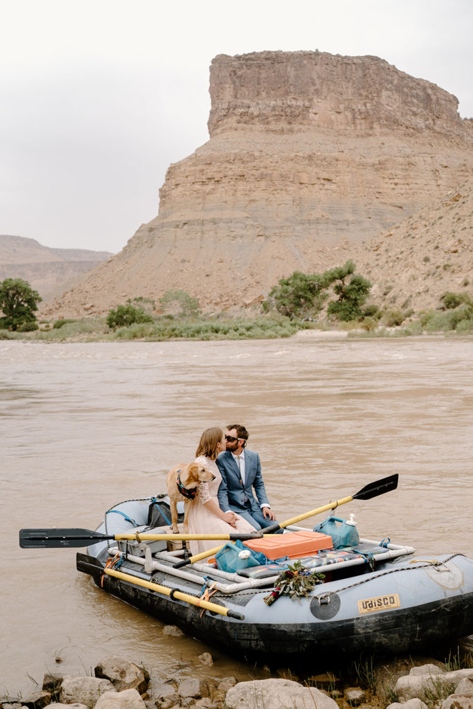 A couple and their dog hop on their raft during their rafting adventure elopement on the Colorado River. 