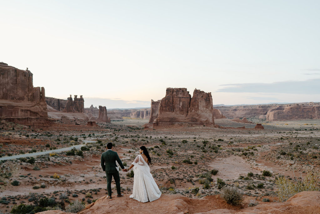 A bride and groom look out over the desert during a beautiful sunrise moment. 