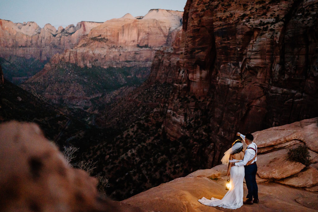 A bride and groom embrace as they look out over Zion National Park during their sunrise elopement ceremony.