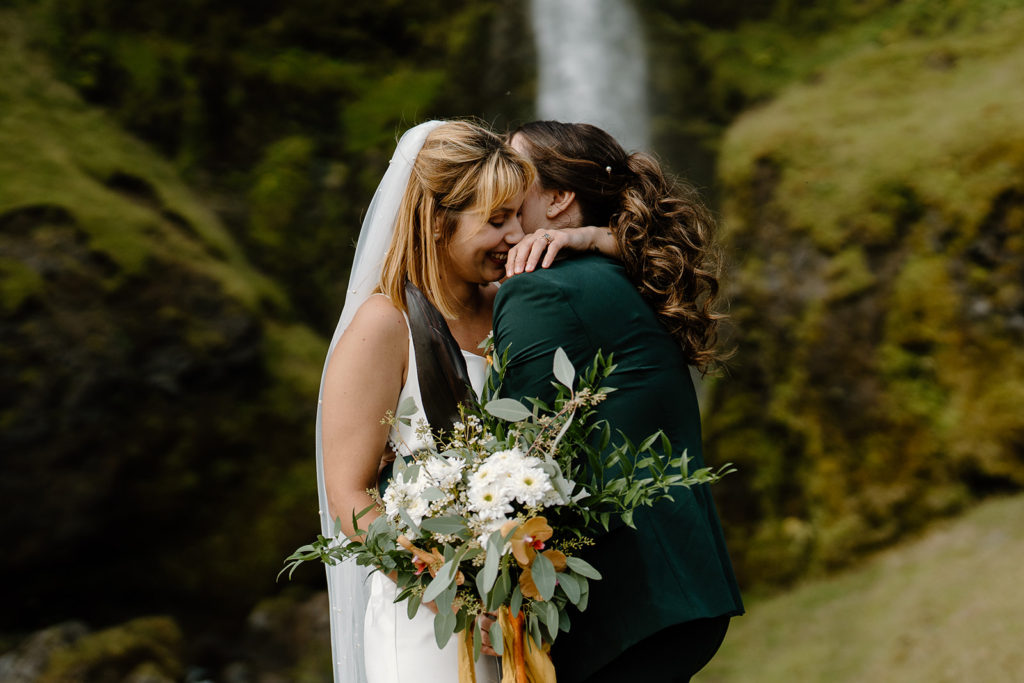 A couple leans in close for a kiss with an Icelandic waterfall behind them on their two-day elopement adventure. 